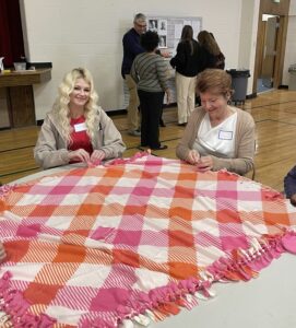Two women sitting at a table tying a blanket