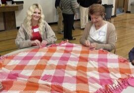 Two women sitting at a table tying a blanket